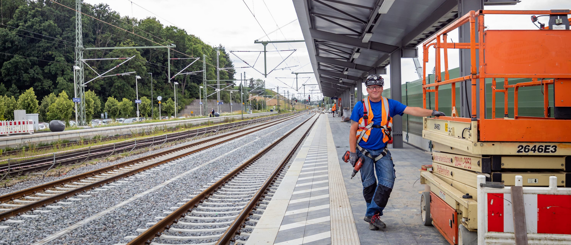 Person steht auf Bahnsteig in Arbeitsklamotten.
